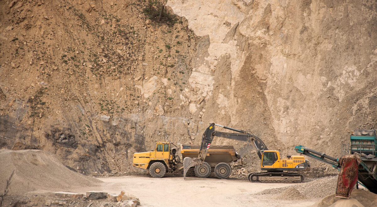 Excavator near factory equipment in a quarry. Earn your mineral rights ownership.