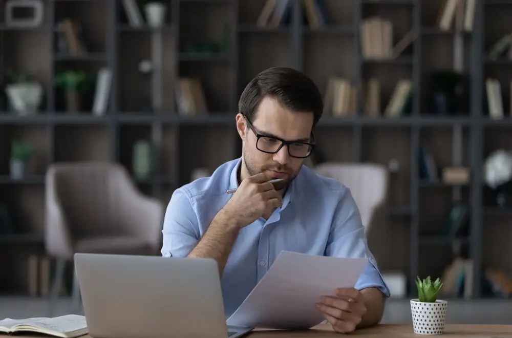 Man in blue shirt intently reviewing documents on mineral rights appraisal and mineral rights value on his laptop in a home office setting.