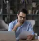 Man in blue shirt intently reviewing documents on mineral rights appraisal and mineral rights value on his laptop in a home office setting.