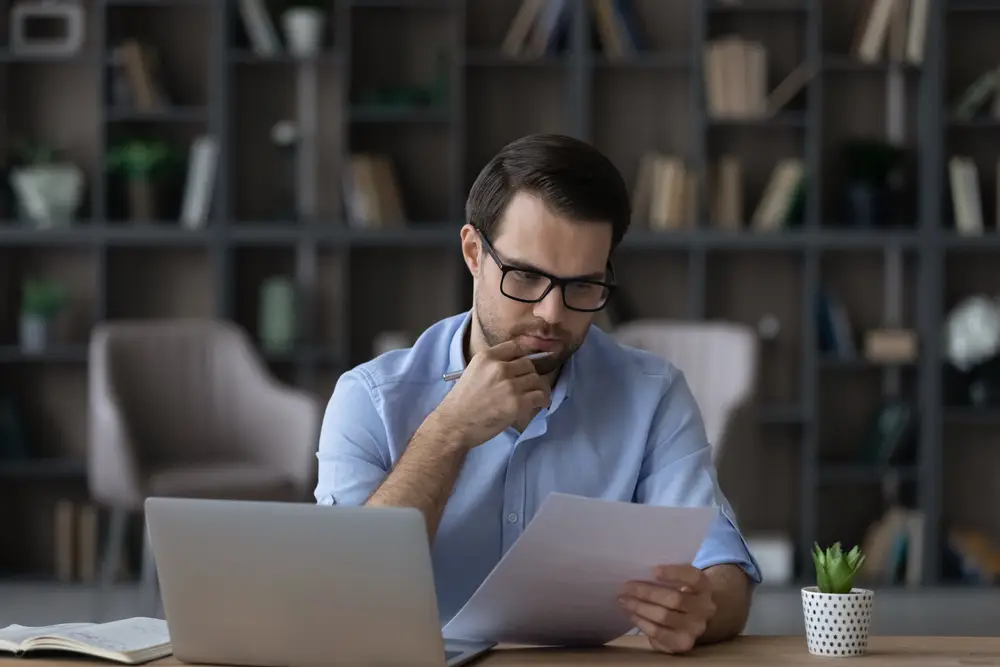 Man in blue shirt intently reviewing documents on mineral rights appraisal and mineral rights value on his laptop in a home office setting.